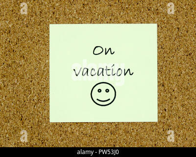 A yellow sticky note with on vacation written on it on a cork board background Stock Photo