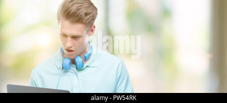 Young handsome blond man using a laptop scared in shock with a surprise face, afraid and excited with fear expression Stock Photo