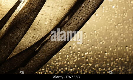 Net fabric draped in front of a rain droplet covered glass window Stock Photo
