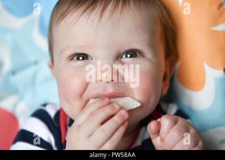 One year old Alexander James eats a banana wafer in a high chair Stock Photo