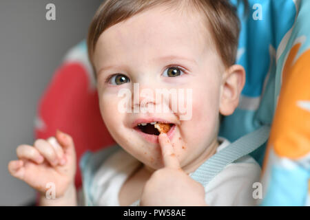 One year old Alexander James eats peanut butter on toast in a high chair Stock Photo