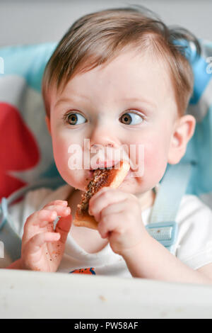 One year old Alexander James eats peanut butter on toast in a high chair Stock Photo