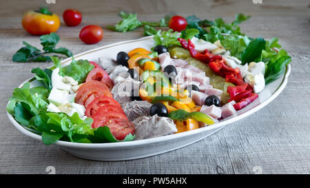 A popular dish of American cuisine - Cobb salad, consisting of greens, eggs, tomatoes, cheese, meat products, stacked in rows on a wide dish and poure Stock Photo