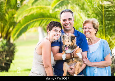 Family group of caucasian happy people with different ages from 30 to 80 years old and nice funny shetland puppy dog with them. love and friendship co Stock Photo