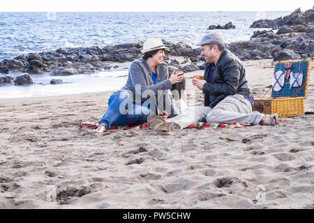 nice middle age caucasian couple happy have fun at the beach doing picnic together in outdoor sea leisure activity. family enjoying love and relations Stock Photo