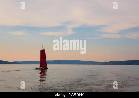 A large red buoy marks the entrance of Cayuga Inlet off Cayuga Lake, in Ithaca, New York State in the Finger Lakes Region during a calm sunset. Stock Photo