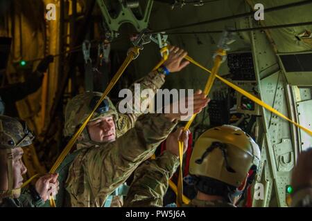 A Jumpmaster assigned to 1st Battalion, 10th Special Forces Group (Airborne), takes the static lines from Paratroopers as they jump from a C-130 Hercules during an airborne operation near Stuttgart, Germany, Sept. 20th, 2017. The jump demonstrates Group’s ability to lead airborne operations in the European theater. Airborne insertions are one of the many infiltration platforms available to Special Operations Forces when responding to a crisis. Stock Photo