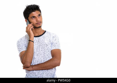 Studio shot of young handsome Indian man talking on mobile phone Stock Photo