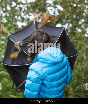 Kidderminster, UK. 12th October, 2018. UK weather: it's very wet and windy! Milder temperatures may be tempting us outdoors, but visitors to a park in Kidderminster have to brave heavy spells of rain and increasingly strong, gusting winds this morning. A woman is struggling in the windy weather with her umbrella inside out. Credit: Lee Hudson/Alamy Live News Stock Photo