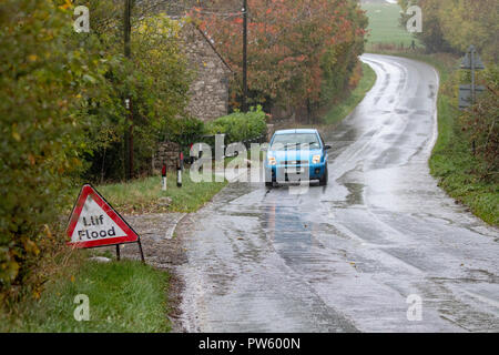 Flintshire, North Wales, 13th October 2018. UK Weather: Heavy rain for most today with weather warnings in place and flood warnings for parts of Wales. A car travelling on the wrong side of the road to dodge flood waters along a rural road near to the village of Lixwm, Flintshire  © DGDImages/AlamyNews Stock Photo