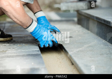 Contractor laying new paving bricks or stones, close up view of his gloved hands. Stock Photo