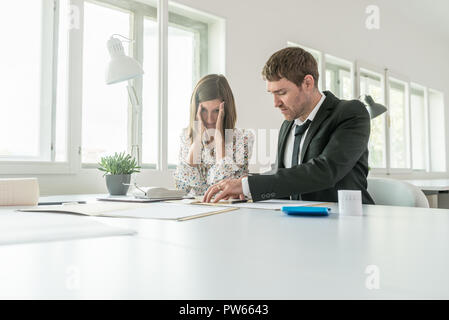 Harassed businesswoman checking the accounts with her male business partner as they sit at a table in the office using a manual adding machine in a lo Stock Photo