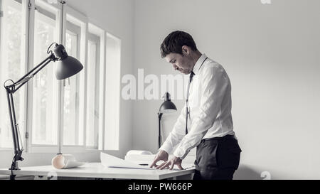 Retro toned image of a businessman analyzing plans while working at his desk in a modern office. Stock Photo