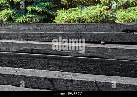 Set of new creosote impregnated wooden sleepers are stacked on each other against the background of green spruce. Railway industry and transport infra Stock Photo