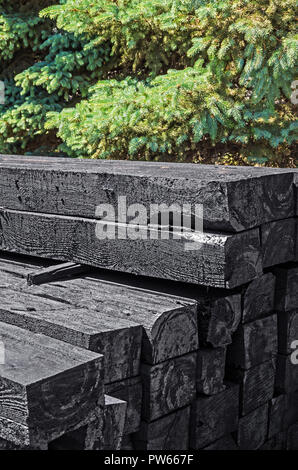 Set of new creosote impregnated wooden sleepers are stacked on each other against the background of green spruce. Transport infrastructure and railway Stock Photo