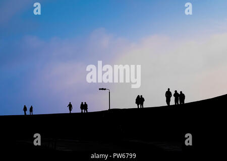 People seen in silhouette walking along the top of The Cobb in the coastal town of Lyme Regis in Dorset. Stock Photo