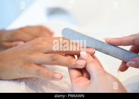 Close-up of a woman in a nail salon receiving a manicure by a beautician with. Beautician file nails to a customer. Stock Photo