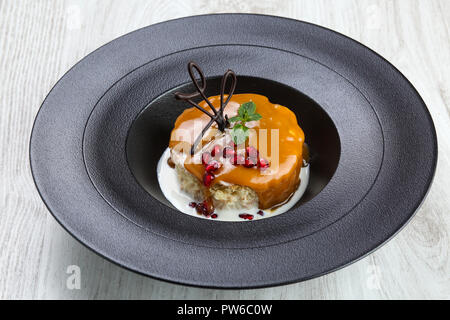 Milky cake in plate with caramel topping and chocolate and mint leaf and pomegranate decoration. Stock Photo