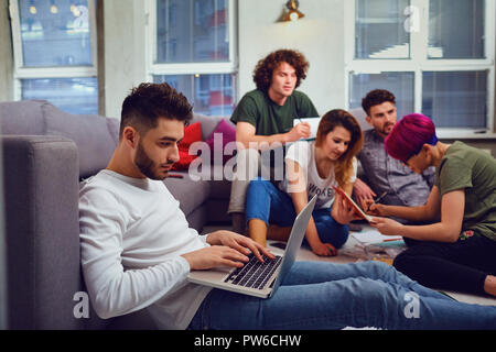 A guy is a student with a laptop on the background of friends. Stock Photo