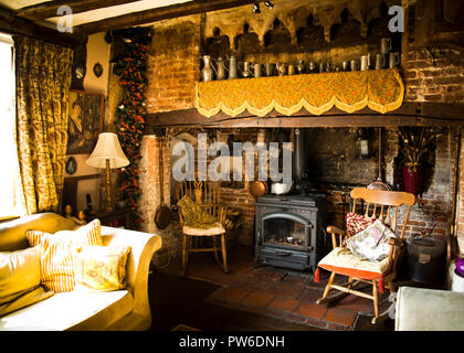 Old fireplace in the drawing room of an old country village house surrounded with decorative antique furniture and interesting objects hanging on wall Stock Photo