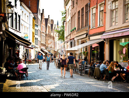 young and elderly couples walking through cobbles street with cafes and shops on both sides of pedestrian only precinct, brugge Belgium, Europe. Stock Photo