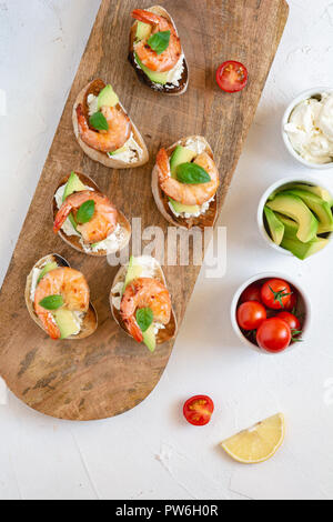 Bruschetta italian snack sandwiches with shrimps, avocado and cheese decorated by basil. Stock Photo