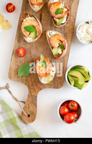 Bruschetta italian snack sandwiches with shrimps, avocado and cheese decorated by basil. Stock Photo