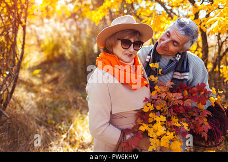 Senior couple walking in autumn forest. Middle-aged man and woman hugging and chilling outdoors. People holding basket for picnic Stock Photo