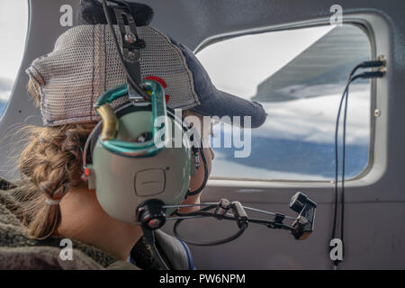 Female passenger looks out the window while flying in an Alaskan Bush Plane, wearing a headset Stock Photo