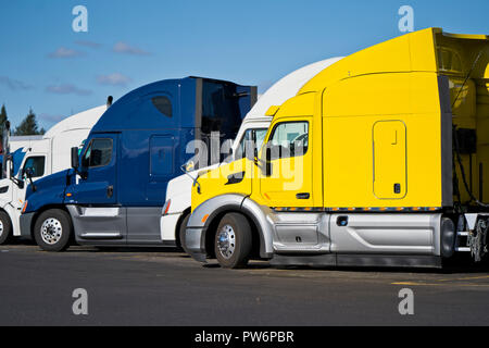 Bright big rigs semi trucks of different makes and models standing in row on truck stop expecting the continuation of traffic on the routes of movemen Stock Photo