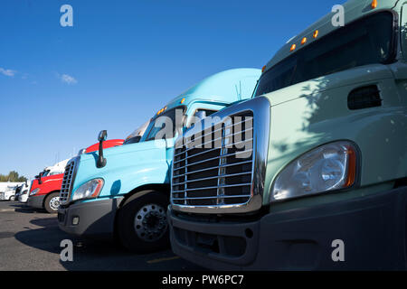 Modern big rigs semi trucks of different makes and models standing in row on truck stop expecting the continuation of traffic on the routes of movemen Stock Photo
