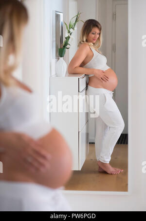 Woman in her ninth month pregnant, looks at herself in the mirror, Germany Stock Photo