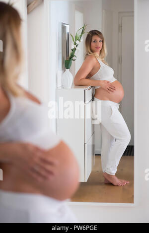 Woman in her ninth month pregnant, looks at herself in the mirror, Germany Stock Photo