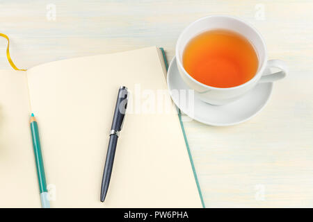 A photo of an open journal with a pen, a pencil, and a cup of tea on a light background, elegant notebook Stock Photo