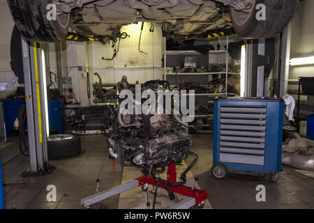 A sports car raised on a lift for repair and under it a detached engine ...