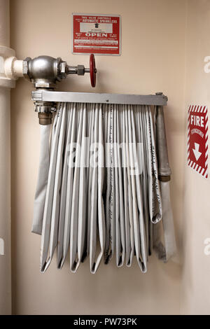 White cloth hose hanging and ready for a fire hazard with big white painted water pipes and red turn value Stock Photo