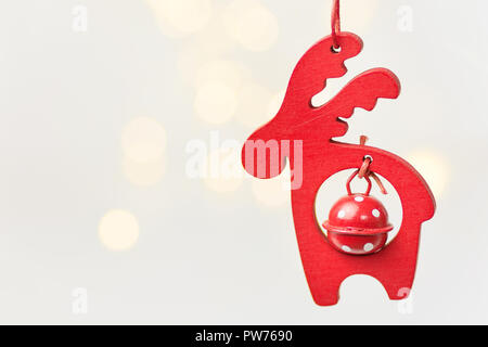 Wooden Christmas ornament red deer with bell hanging on white background with golden garland bokeh lights. Pastel colors. Magic holiday atmosphere. Cl Stock Photo