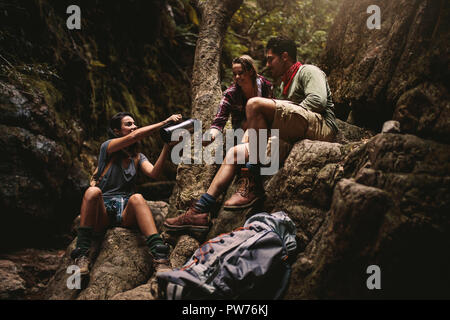 Woman serving coffee to female friend sitting on rocks. Friends taking coffee break while hiking in rocky mountain. Stock Photo