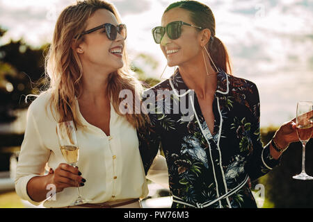 Fashionable young women with wine walking outdoors and smiling. Two women walking together with glass of wine. Stock Photo