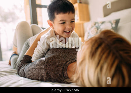 Cute little kid playing with his mother on bed. Mother and son having a fun time at home. Stock Photo