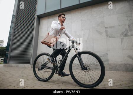 Side view of an entrepreneur commuting to office on a bike. Man wearing office bag riding a bicycle in street going to office. Stock Photo