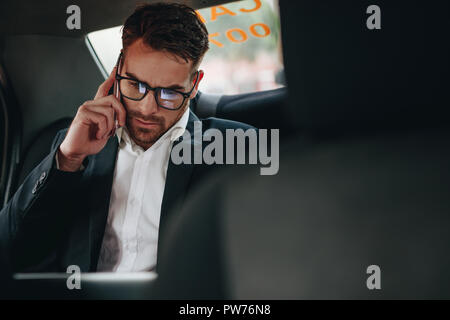 Businessman doing office work while commuting to office in a taxi. Entrepreneur managing business work on the move sitting in a car. Stock Photo