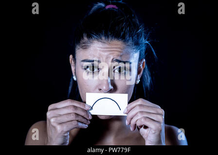 Close up portrait of sad attractive young latin woman suffering from depression in dramatic lighting isolated on black background. Stock Photo