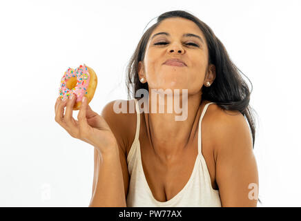 Portrait of extremely happy beautiful latin young woman eating a delicious donuts enjoying it with pleasure in give yourself a treat and forgetting di Stock Photo