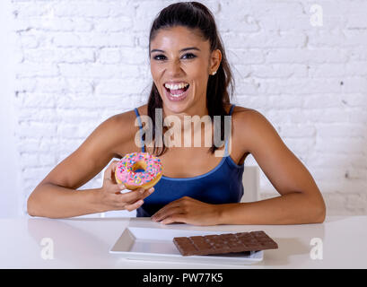 Young attractive latin woman sitting at table about to eat chocolate and doughnuts looking excited and happy in no more diet, sugar and chunky unhealt Stock Photo