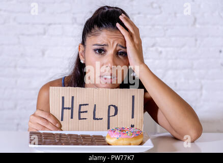 Young worried latin woman feeling tempted and guilty wanting to eat chocolate and donuts asking for help in diet calories sugar addiction nutrition an Stock Photo