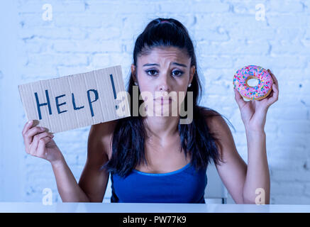 Young worried latin woman feeling tempted and guilty wanting to eat chocolate and donuts asking for help in diet calories sugar addiction nutrition an Stock Photo