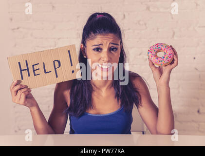 Young worried latin woman feeling tempted and guilty wanting to eat chocolate and donuts asking for help in diet calories sugar addiction nutrition an Stock Photo