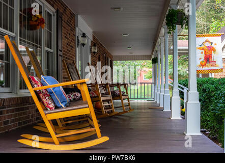 Rocking chairs lined up on long front porch. Red barn is in the background. Stock Photo