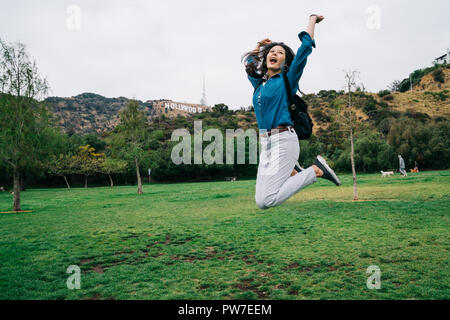 female traveler joyfully jumping and raising her hands in the sky. Carefree young girl happily travel in national park. pretty lady dancing in freedom Stock Photo